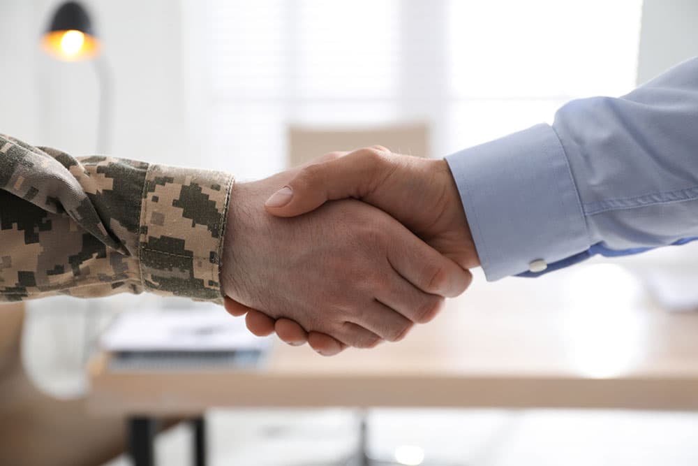 A soldier and a businessman engage in a handshake, representing partnership and mutual respect between their fields.