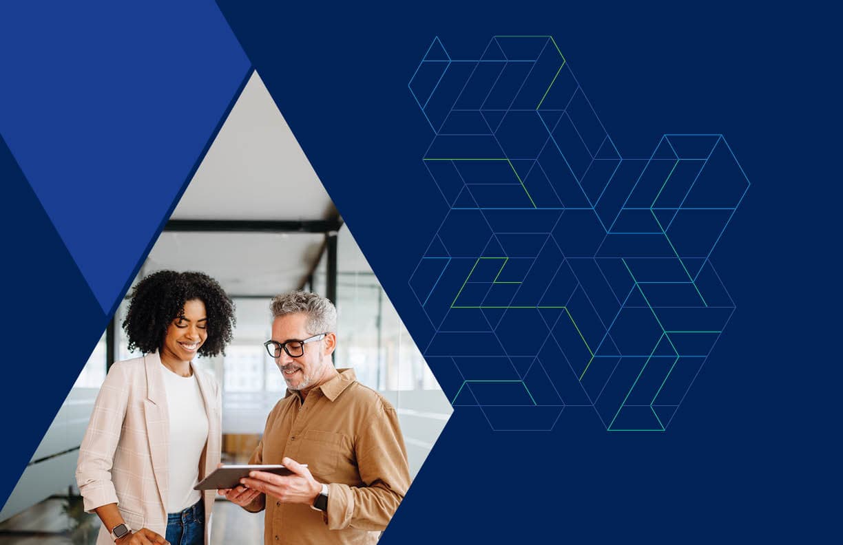 In an office, a businesswoman and man examine a tablet, discussing their work together.