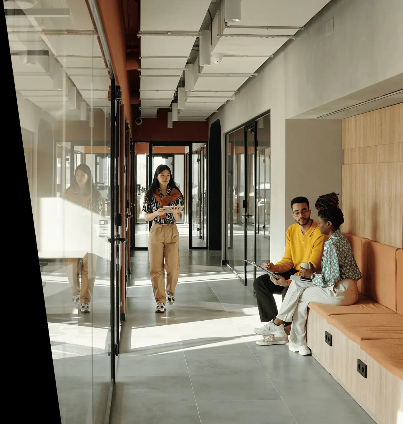 People sitting on benches in a modern office building, engaged in conversation and working on laptops.