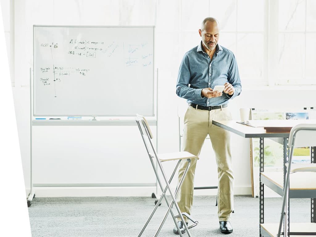 Man standing in his office checking his phone.