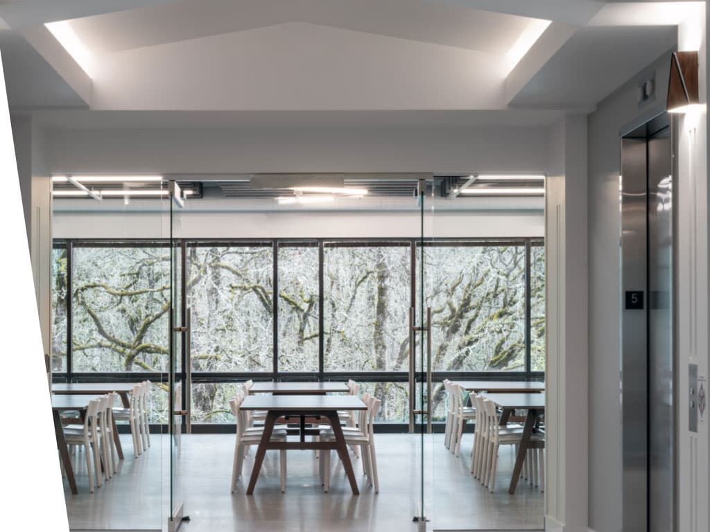 A cozy room featuring several tables and chairs, with natural daylight streaming through a window. The walls are adorned with cabinetry, and a sink fixture is visible, contributing to the overall interior design of the space.