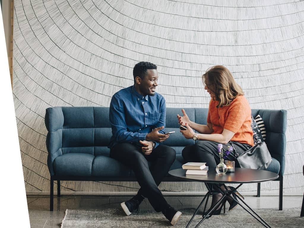 Man and woman on a office sofa talking.