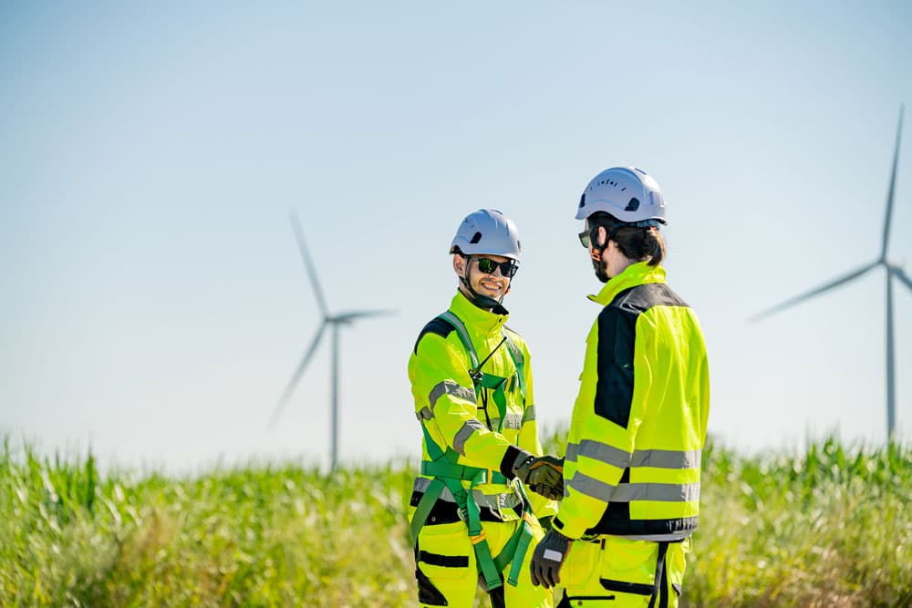 Two men in yellow safety gear positioned by wind turbines, highlighting the importance of building strong partnerships.