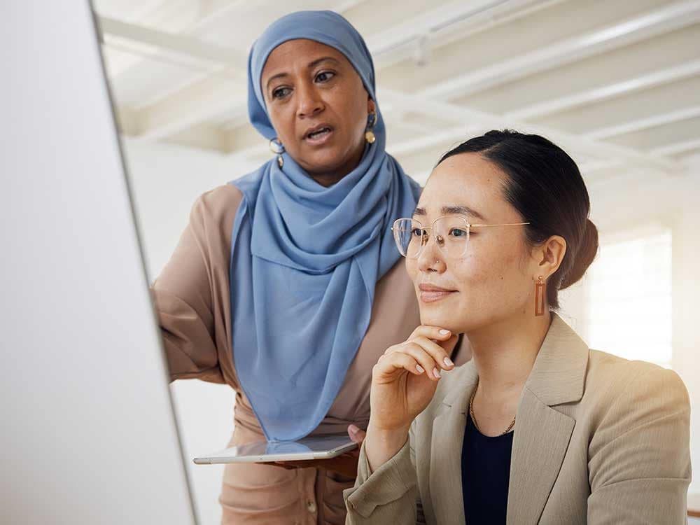 A woman with a scarf is smiling while looking at a computer screen in an indoor setting.