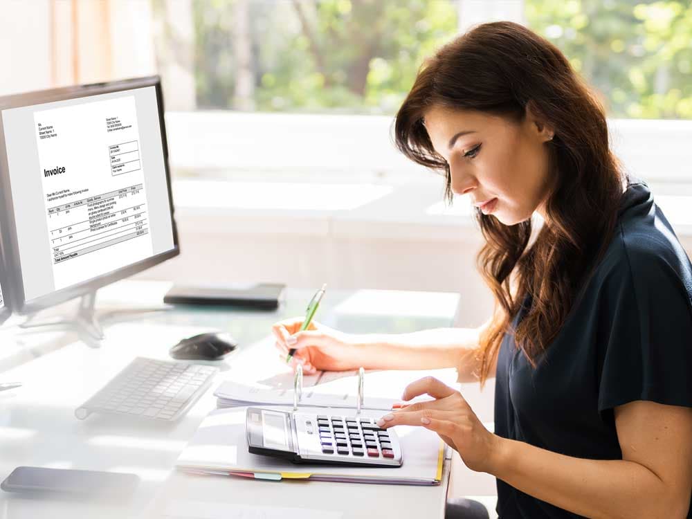 A woman sitting at a desk with a laptop, wearing casual clothing, indoors.