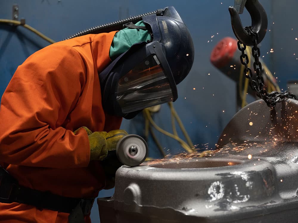 A man in an orange jacket is welding metal pieces together.