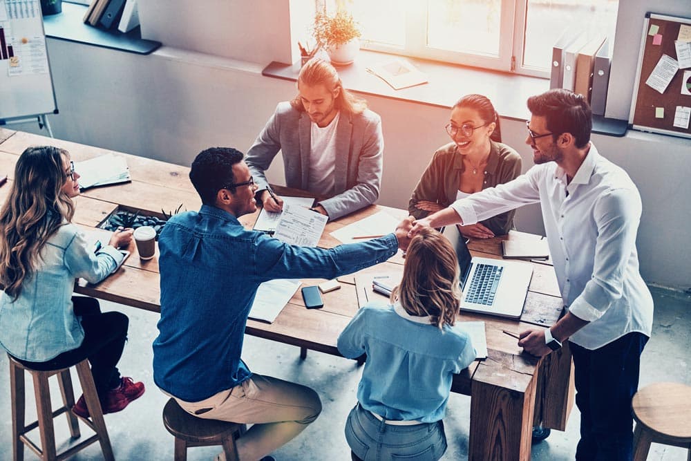 A group of colleagues sitting at a table with laptops, promoting teamwork in a positive and inclusive work setting.